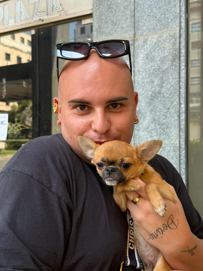 Un ragazzo stringe a sé il suo chihuahua fulvo davanti a una vetrina in città