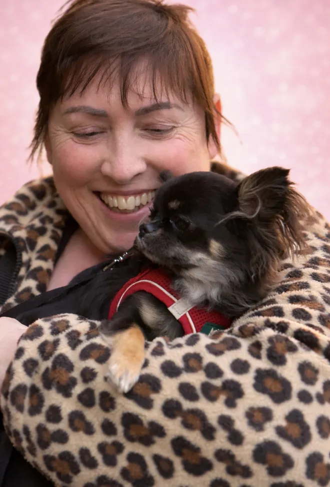 Una signora sorride alla sua chihuahua black and tan avvolta in una coperta